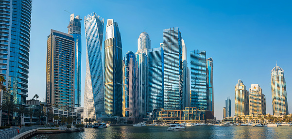 Dubai, United Arab Emirates - April 9, 2023: Panoramic view at futuristic and modern skyscraper skyline of Dubai marina with a large promenade and many yachts in the creek calm water in Dubai, United Arab Emirates on a clear blue sky day with nice Dubai winter and spring weather
