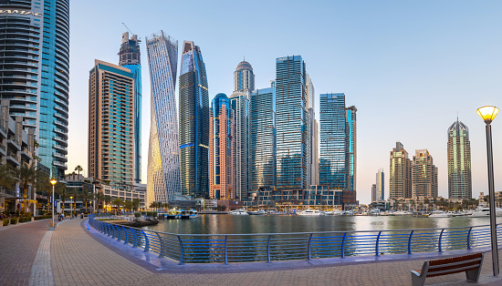 Dubai, United Arab Emirates - April 9, 2023: Panoramic view at Futuristic and modern skyscraper skyline of Dubai marina with a large promenade and many yachts in the creek calm water in Dubai, United Arab Emirates at dusk