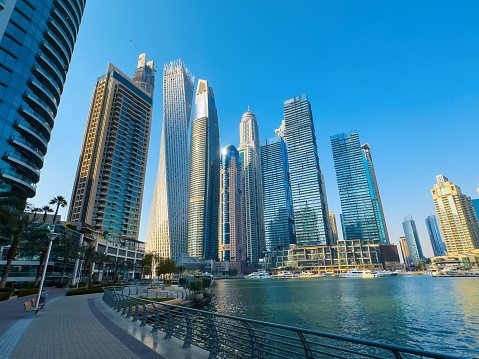 Futuristic and modern skyscraper skyline of Dubai marina with a large promenade and many yachts in the creek calm water in Dubai, United Arab Emirates on a clear blue sky day with nice Dubai winter and spring weather