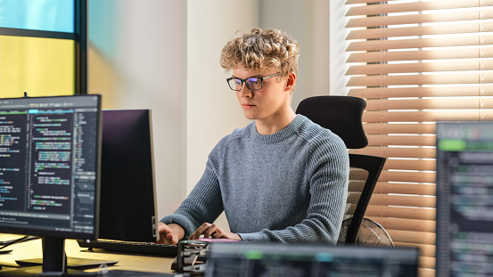 Male Software Engineer Coding On Desktop Computer in Creative Office Space. Young Caucasian Man Applying His Programming Skills in Innovative Technological Startup. Junior Developer Working.