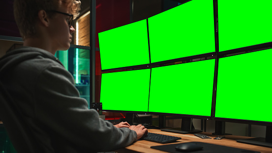 Young Caucasian Man Writing Code on Professional Six Monitors Setup With Green Screen Chromakey. Male Cyber Security Expert Controlling Data Protection System in International Intelligence Agency.