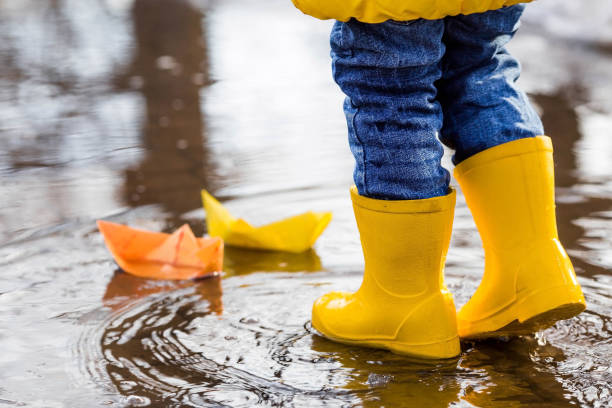 istock It's springtime. A small child in yellow rubber boots jumps through puddles, plays and launches paper boats on the water.. Photo of spring and autumn holidays. The concept of spring. 1481186616