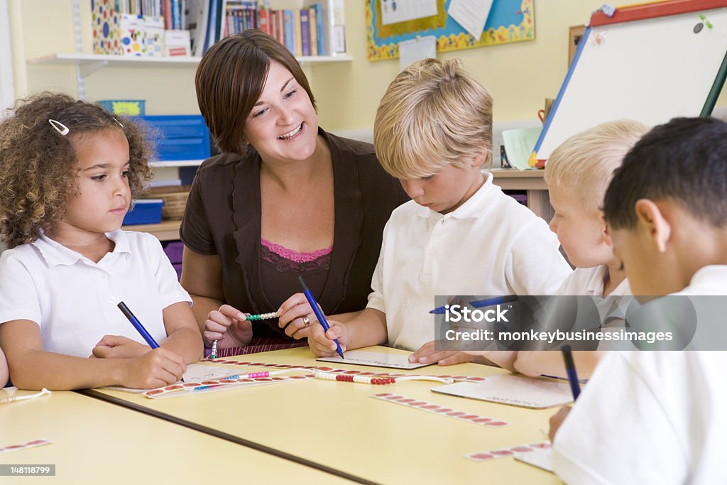 Teacher with young learners in classroom Schoolchildren and their teacher in a primary class concentrating Mathematics Stock Photo