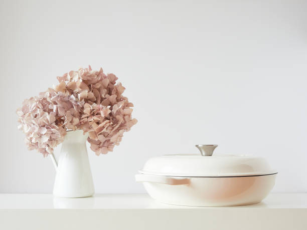 istock Elegant and simple table with white pot and vase with dried pink hydrangea flowers. Front view with copy space on off-white wall background. 1481193158