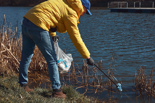 Volunteer and environmental activist cleaning dirty lake shore filled with trash.