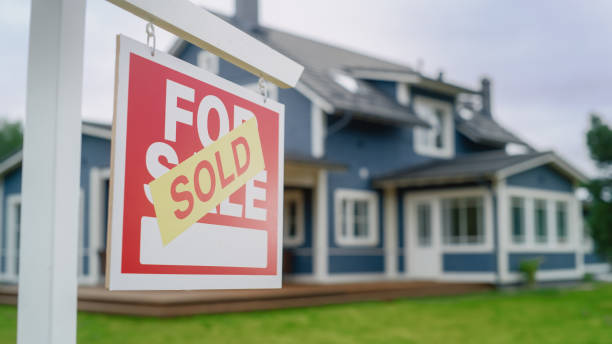 close up of a house sold sign on a lawn in front of a big modern house with traditional architecture. housing market concept with residential property in the countryside. - sold imagens e fotografias de stock