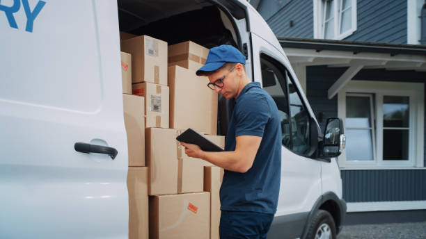 corriere che utilizza il tablet computer accanto alla porta laterale del furgone di consegna aperta con pacchi di cartone. postino consegna il pacco a un proprietario di casa. - delivery van foto e immagini stock