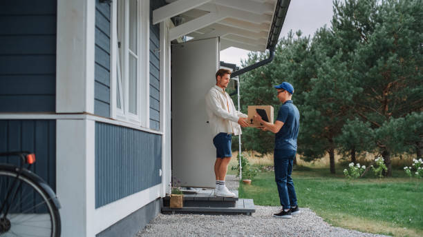 istock Handsome Young Homeowner Receiving an Awaited Parcel from a Cheerful Courier. Postal Service Worker Comes to the House to Make a Door to Door Delivery and Get a POD Signature on Tablet. 1481194555
