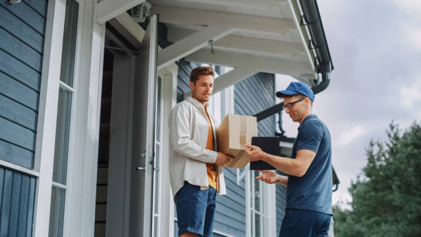 handsome young homeowner receiving an awaited parcel from a cheerful courier. postal service worker comes to the house to make a door to door delivery and get a pod signature on tablet. - pod imagens e fotografias de stock