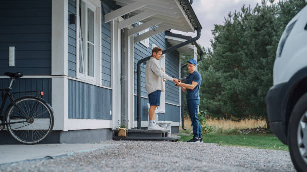 istock Handsome Young Homeowner Receiving an Awaited Parcel from a Cheerful Courier. Postal Service Worker Comes to the House to Make a Door to Door Delivery and Get a POD Signature on Tablet. 1481194888