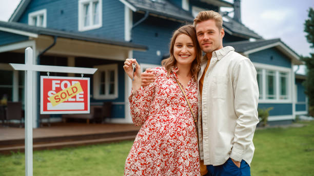 Portrait of a Beautiful Young Couple in Love Standing in Front Their New Home. Successful Homeowners Looking at Camera and Smile. Female in a Dress Expecting a Baby. Real Estate Housing Market Concept Portrait of a Beautiful Young Couple in Love Standing in Front Their New Home. Successful Homeowners Looking at Camera and Smile. Female in a Dress Expecting a Baby. Real Estate Housing Market Concept fresh start stock pictures, royalty-free photos & images