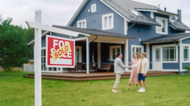 istock Young Couple Visiting a Potential New Home Property , SHaking Hands with Professional Real Estate Agent. Female real estate agent Showing the Area to Future Homeowners. Focus on Sold Sign. 1481196149