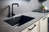 Kitchen sink area with black square matte sink tap in contemporary style. Matte black and stoneware kitchen design. Black ceramic sink with gas hob and oven in background.