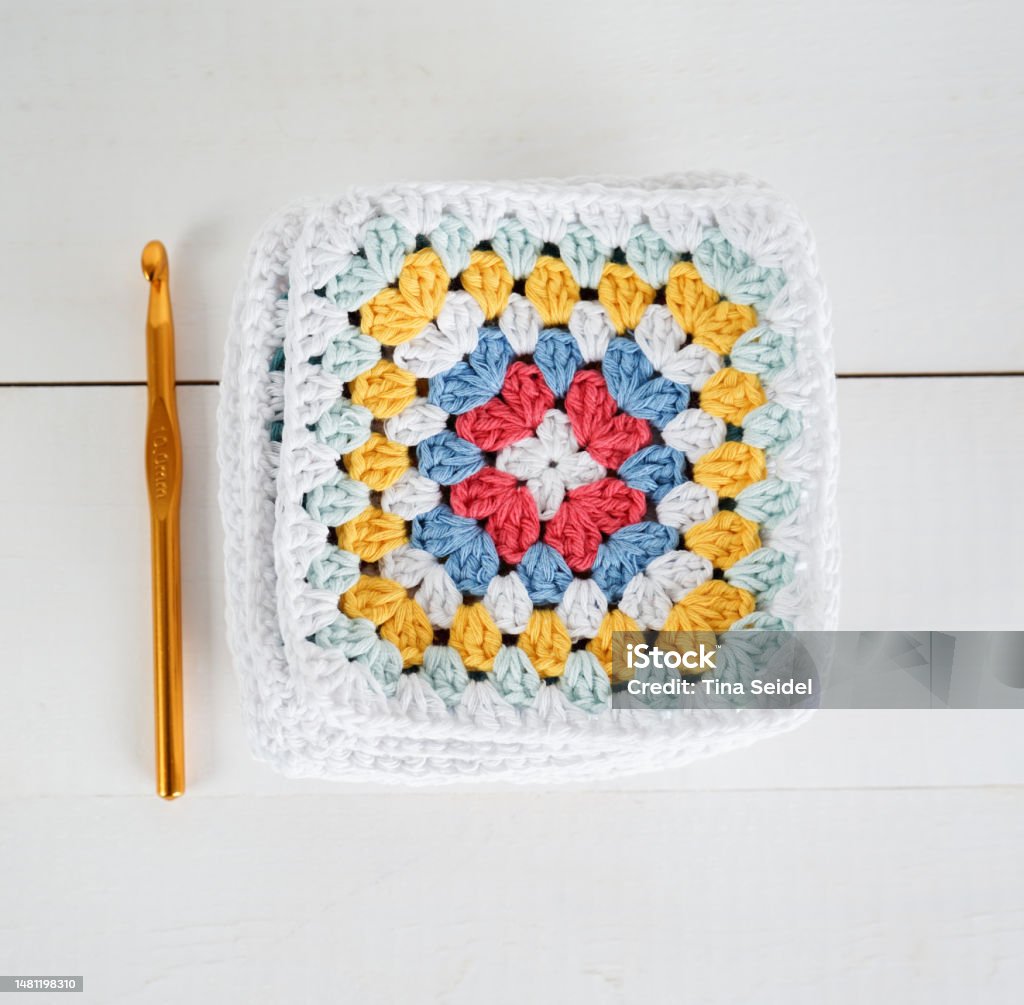 multicolored granny squares with crochet hook and white wooden ground multicolored granny squares with crochet hook and white wooden ground handmade Blanket Stock Photo