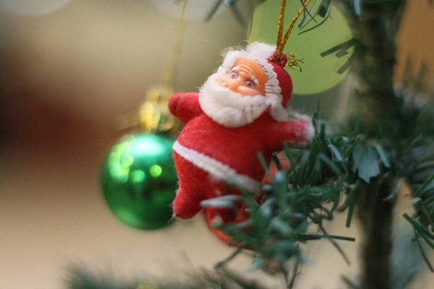 Santa Claus in front of a Christmas tree, a Santa Claus on Christmas tree picture shows a decorated Christmas tree with Santa Claus figurines or ornaments placed on the tree. The tree might be a real or artificial tree, decorated with lights, garlands, and various ornaments, such as balls, stars, or candy canes. small, cartoonish figurines realistic depictions of Santa Claus. festive and joyful conveying the spirit of Christmas and the excitement of the holiday season