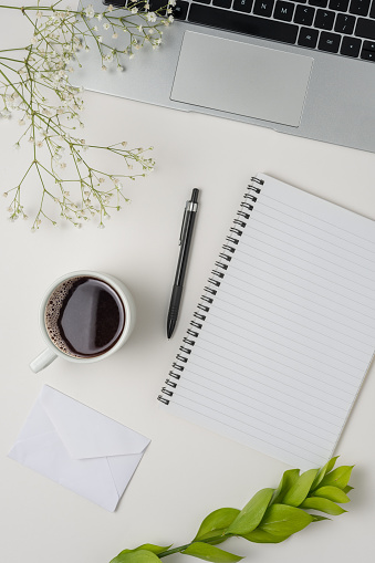 Flat lay, top view office table desk. Workspace with blank clip board, laptop, office supplies, pencil, green leaf, and coffee cup on white background.