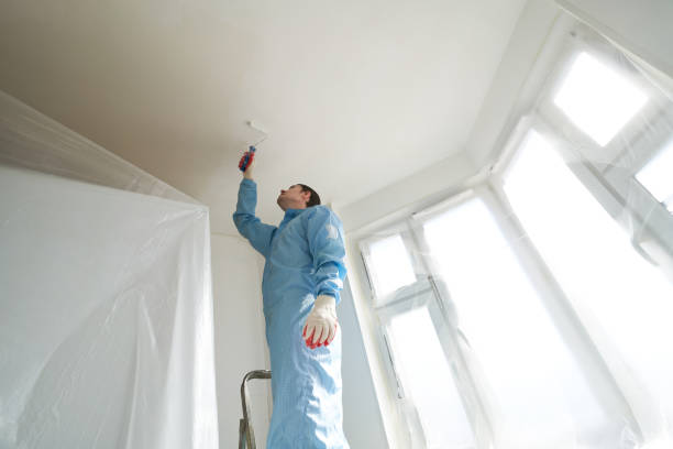 istock Man stands on the stairs and paints the wall with a roller 1481201730