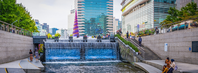 People relaxing along the banks of the Cheonggyecheon Stream flowing between the skyscrapers of central Seoul, South Korea.