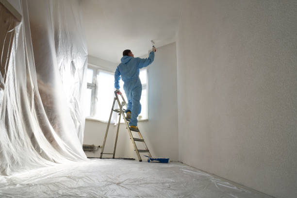 istock Man stands on the stairs and paints the wall with a roller 1481202801