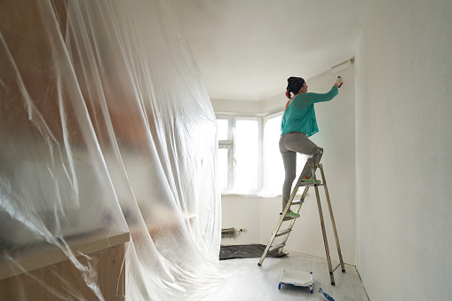 Woman stands on the stairs and paints the wall with a roller. Concept of home makeover and renovation