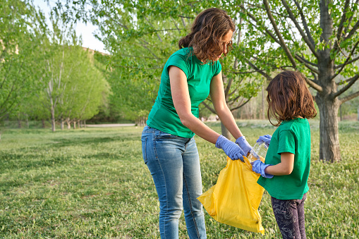 Una niña con su madre recogiendo plástico del campo para cuidar la naturaleza photo