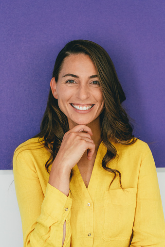 Confident business woman in front of purple background. Smiling mid aged woman in yellow shirt looking at camera. Business woman studio portrait.