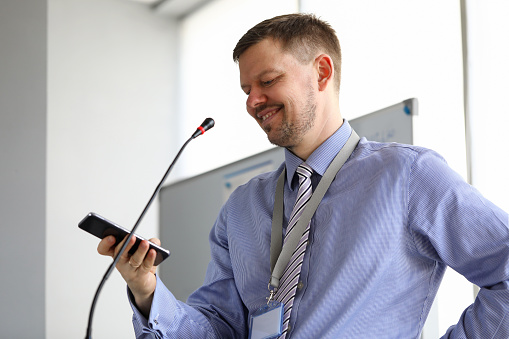 Man speaks into microphone and looks into phone. Speaker presents material at seminar or training. Motivational classroom with microphone. Organization business training seminars