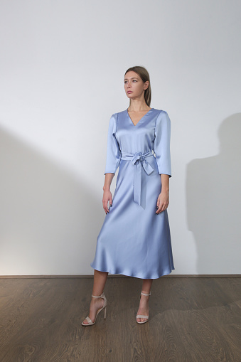 Serie of studio photos of young female model in beautiful blue silk satin midi dress.