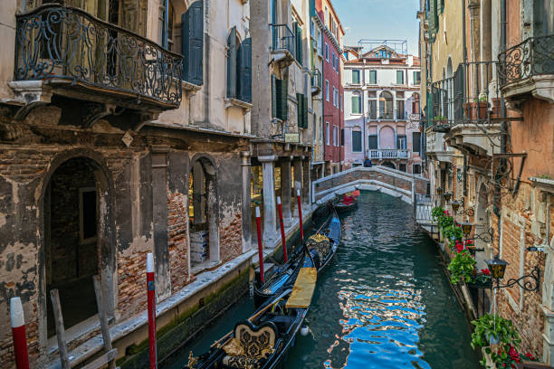 Venice: View from Ponte dei Bareteri over the Rio dei Bareteri canal, Ponte de le Acque bridge and typical Venetian houses on the banks. A gondola in the foreground.