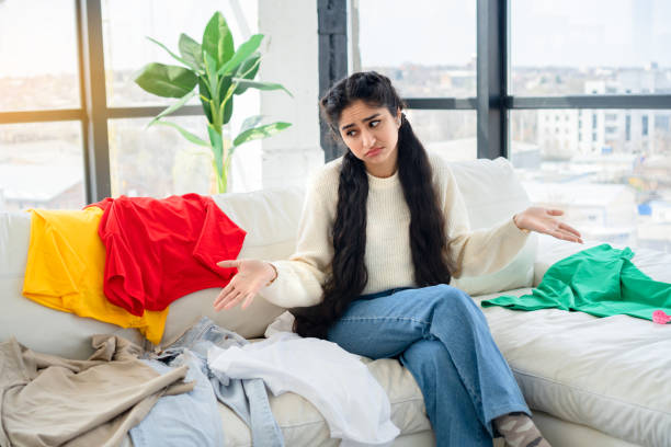 Upset girl who has nothing to wear sits on the couch in modern interior with panoramic windows. stock photo