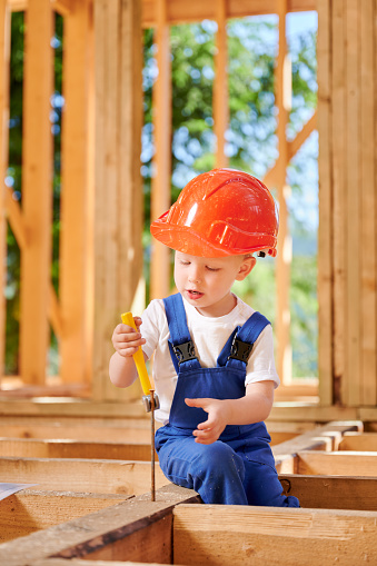 Young boy indulges in playful construction of timber-framed house. Toddler acquiring skill of extracting driven nail with hammer. Concept of early childhood development and parental assistance.