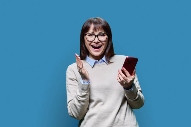 istock Joyful middle aged woman with phone on blue background 1481215510