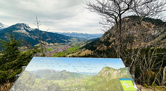 Bad Hindelang, Germany - March, 24 - 2023. View of Bad Hindelang, Ostrach valley in the Oberallgäu region. In the foreground an information board with names and heights of the landscape to be seen.