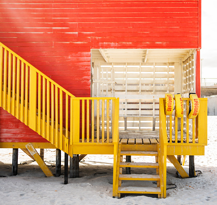 Steps leading to a colorful yellow and red lifeguard hut standing on sandy beach in the summertime