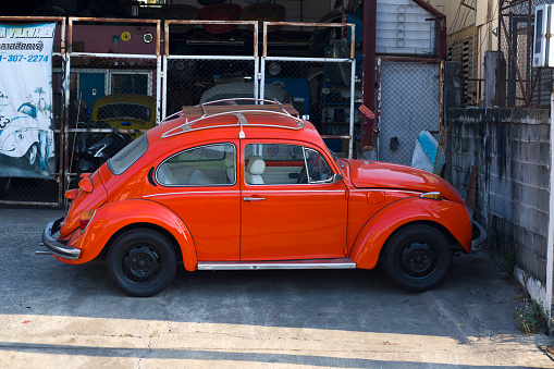 Parked orange Volkswagen oldtimer outside of small auto repair shop for restauration of oldtimers in Bangkok Ladprao