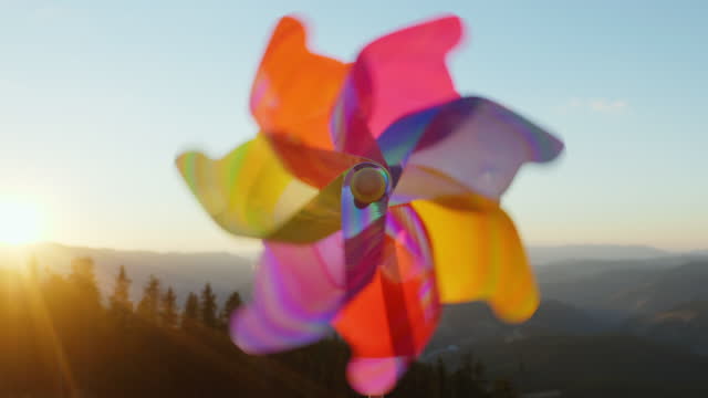 Pinwheel rotate color plastic, windmill with blowing wind meadow of tall grass in mountains on sunny day at sunset in autumn blue sky. Descending bright disk of sun beyond horizon. Relax. Travel
