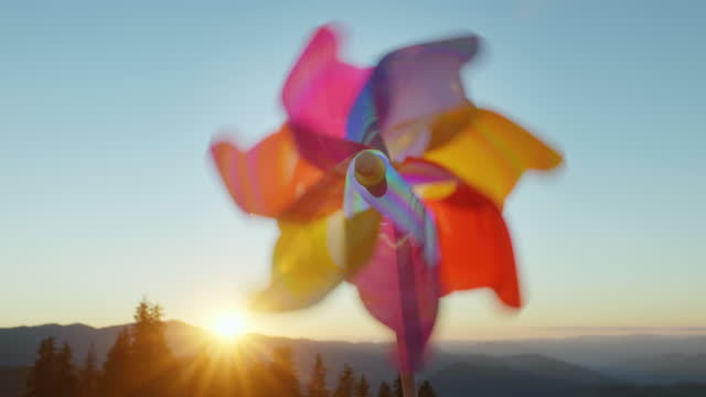 Pinwheel rotate color plastic, windmill with blowing wind meadow of tall grass in mountains on sunny day at sunset in autumn blue sky. Descending bright disk of sun beyond horizon. Relax. Travel