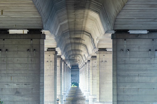 Tunnel from column under road bridge in city. Row pillars and group arches. Built structure prefabricated concrete of overpass. Details architecture of bridge on river. Technology construction.