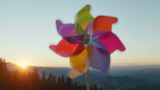 Windmill pinwheel rotate color plastic with blowing wind meadow of tall grass in mountains on sunny day at sunset in autumn blue sky. Descending bright disk of sun beyond horizon. Relax. Travel
