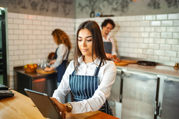 istock Female waitress wearing apron, working on digital tablet behind the bar counter 1481221680