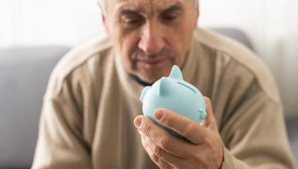 Senior caucasian man holding piggy bank with glasses depressed and worry for distress, crying angry and afraid. sad expression stock photo
