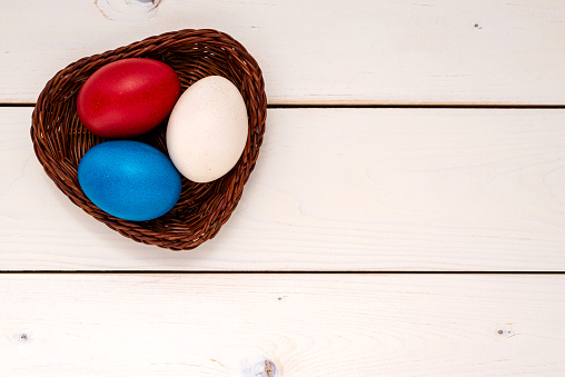 Multicolor decorated Easter eggs in the wicker bowl on a white wooden table. Easter concept.
