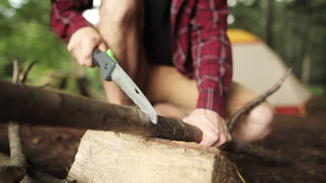 An unrecognisable man cuts a branch with a hand saw at a campsite in the forest on vacation