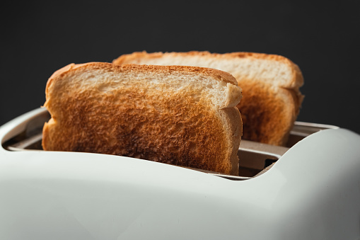 Close-up shot of slightly burnt white bread toasts sticking out of a toaster on the black background. Ready toasts with a dark  crust. Morning breakfast concept