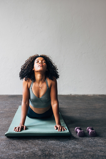 A smiling Latin female athlete stretching on yoga mat.