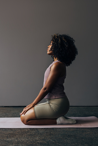 A side view of a serious Latin female athlete keeping her eyes closed while sitting on yoga mat.