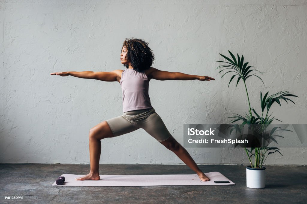 A Beautiful Woman Doing Her Daily Workout A side view of a serious Latin female athlete stretching while standing on yoga mat. Yoga Stock Photo