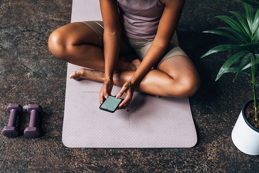 A from above view of an unrecognizable Latin female texting on her mobile phone while sitting on yoga mat.