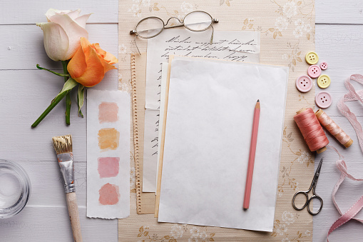 Overhead view of a blank paper with pastel color swatches,brush,glasses and roses