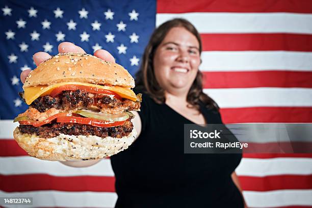 Foto de Gordo Jovem Smilingly Oferece Hambúrguer De Contra Bandeira Dos Eua e mais fotos de stock de Bandeira Norte-Americana